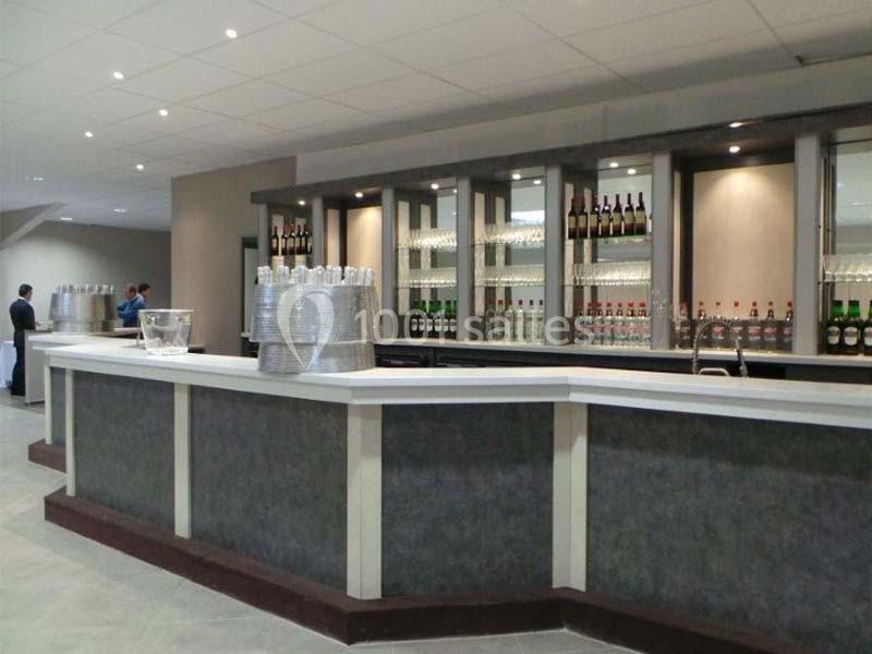 Comptoir de bar moderne avec étagères garnies de bouteilles et verres, dans un espace lumineux et épuré.