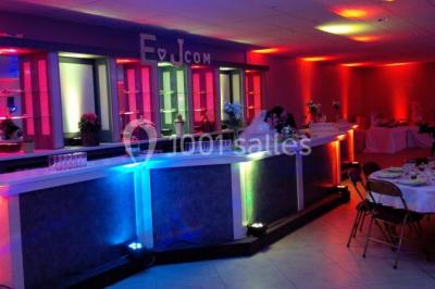 Salle de réception avec bar éclairé par des lumières colorées et invités rassemblés dans une ambiance tamisée.