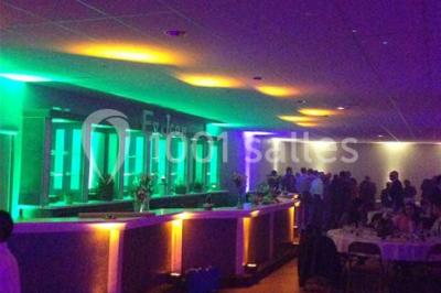 Salle de réception avec bar éclairé par des lumières colorées et invités rassemblés dans une ambiance tamisée.