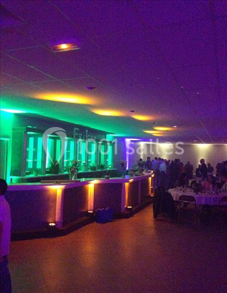 Salle de réception avec bar éclairé par des lumières colorées et invités rassemblés dans une ambiance tamisée.