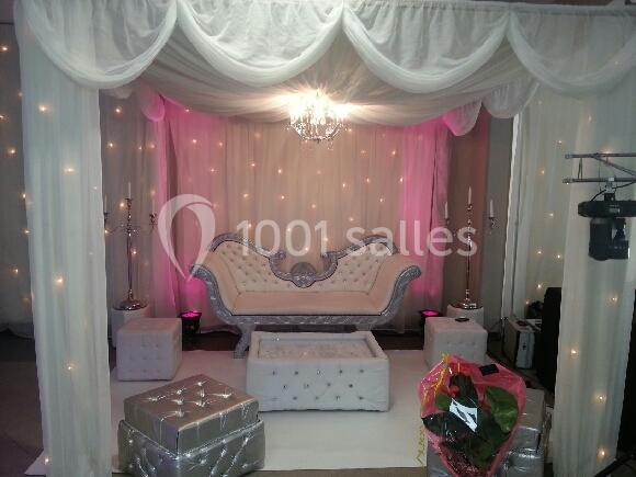 Canapé argenté capitonné entouré de poufs assortis, sous un dais blanc avec rideaux et éclairage tamisé.