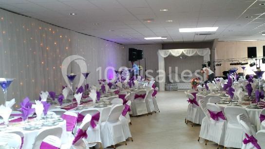 Salle de réception décorée avec des nappes blanches, des nœuds violets sur les chaises et des tables dressées.