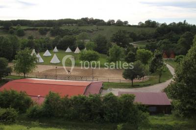 Tente tipi beige installée dans un champ verdoyant sous un ciel bleu, avec une ouverture laissant entrevoir l'intérieur.