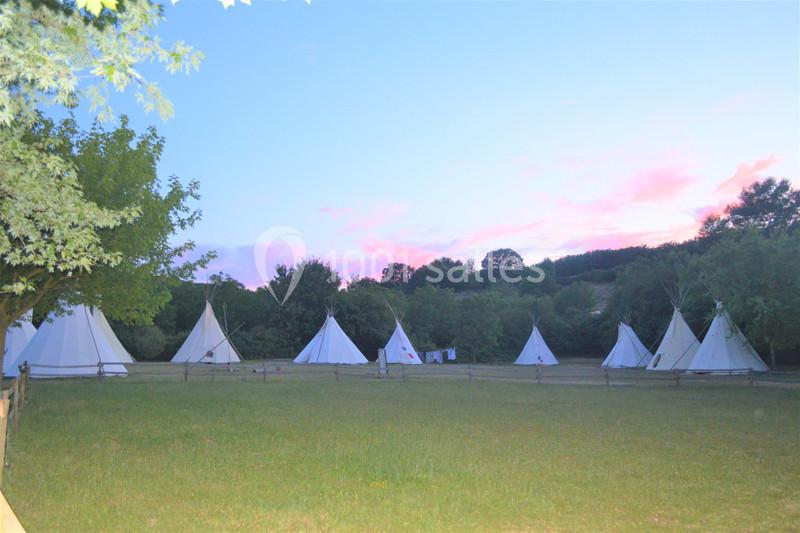 Alignement de tipis blancs sur une pelouse entourée d'arbres, sous un ciel au coucher du soleil.