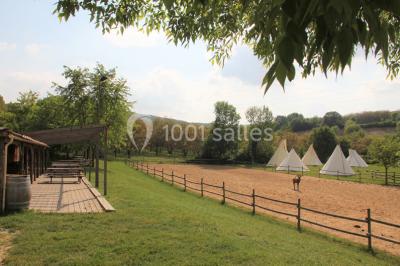 Tente tipi beige installée dans un champ verdoyant sous un ciel bleu, avec une ouverture laissant entrevoir l'intérieur.