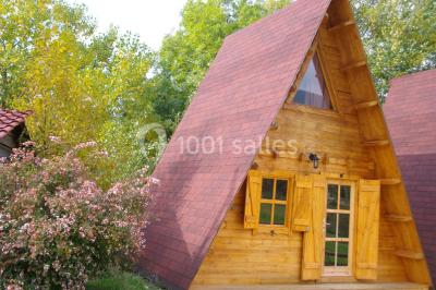 Tente tipi beige installée dans un champ verdoyant sous un ciel bleu, avec une ouverture laissant entrevoir l'intérieur.