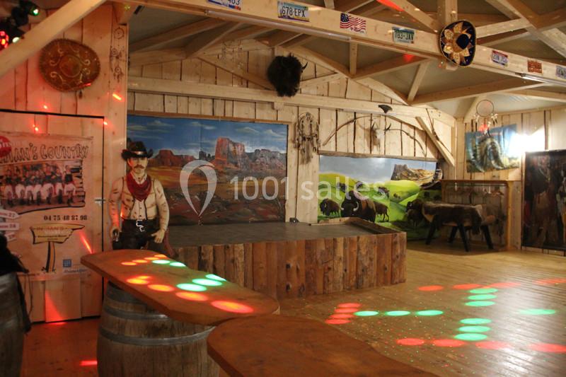 Salle décorée sur le thème western avec des fresques de paysages, des objets rustiques et des lumières colorées au sol.