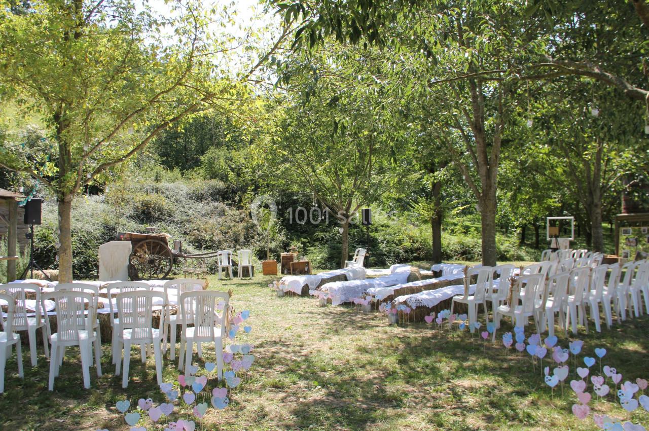 Chaises blanches disposées en extérieur sous des arbres, avec une allée centrale décorée de cœurs en papier colorés.