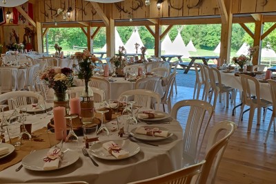 Tente tipi beige installée dans un champ verdoyant sous un ciel bleu, avec une ouverture laissant entrevoir l'intérieur.