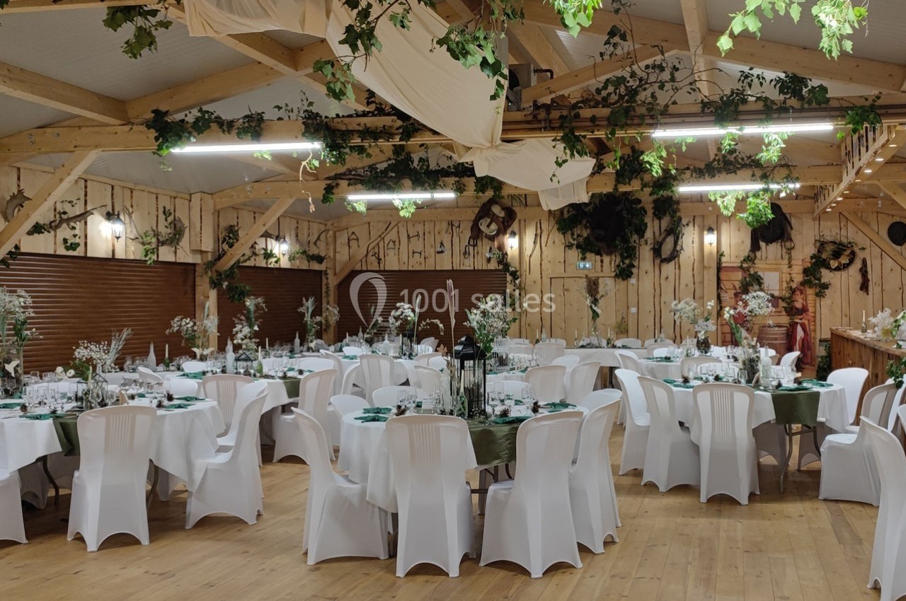 Salle de réception décorée avec des tables rondes, nappes blanches, chaises assorties et ornements végétaux suspendus.