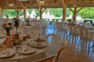 Tente tipi beige installée dans un champ verdoyant sous un ciel bleu, avec une ouverture laissant entrevoir l'intérieur.