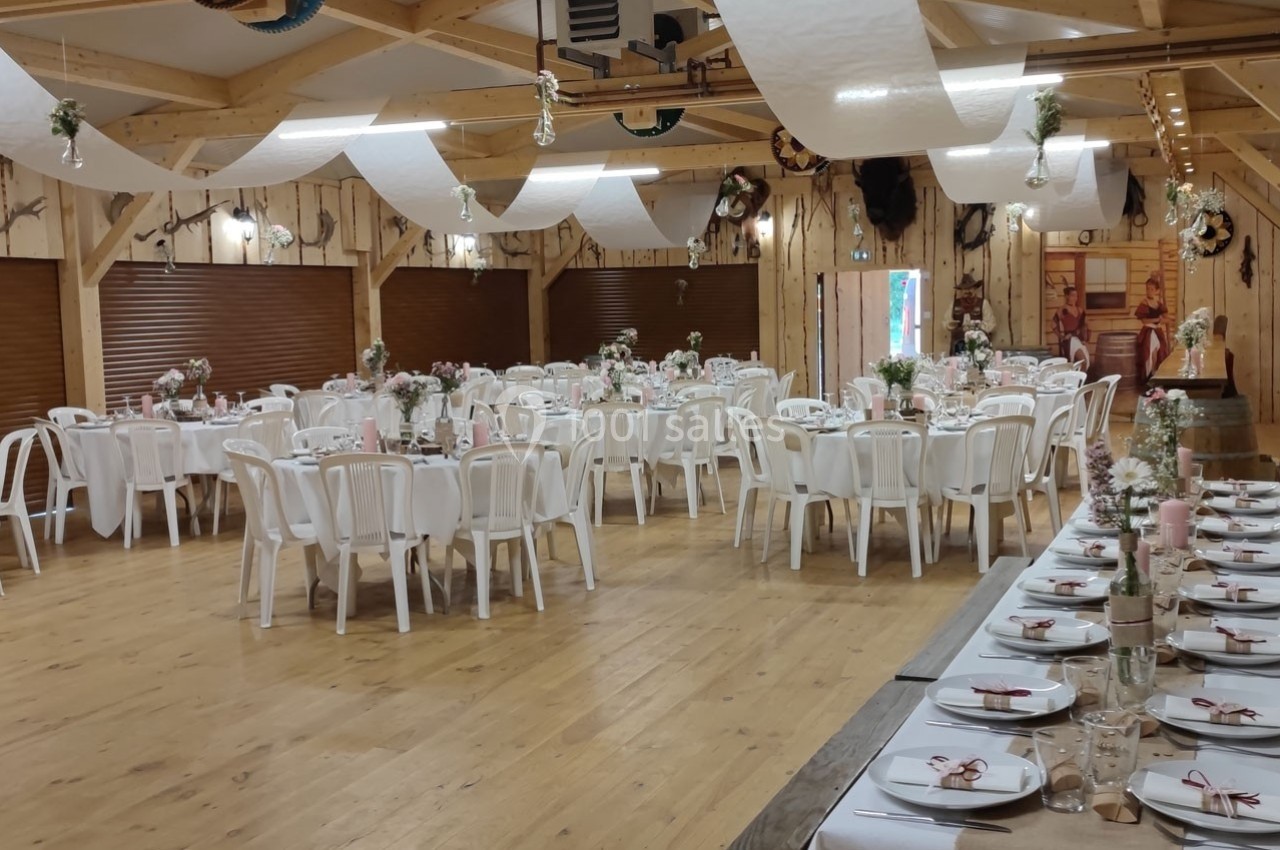 Salle de réception décorée avec des tables rondes et rectangulaires, nappes blanches et ornements floraux.