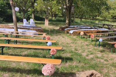 Tente tipi beige installée dans un champ verdoyant sous un ciel bleu, avec une ouverture laissant entrevoir l'intérieur.