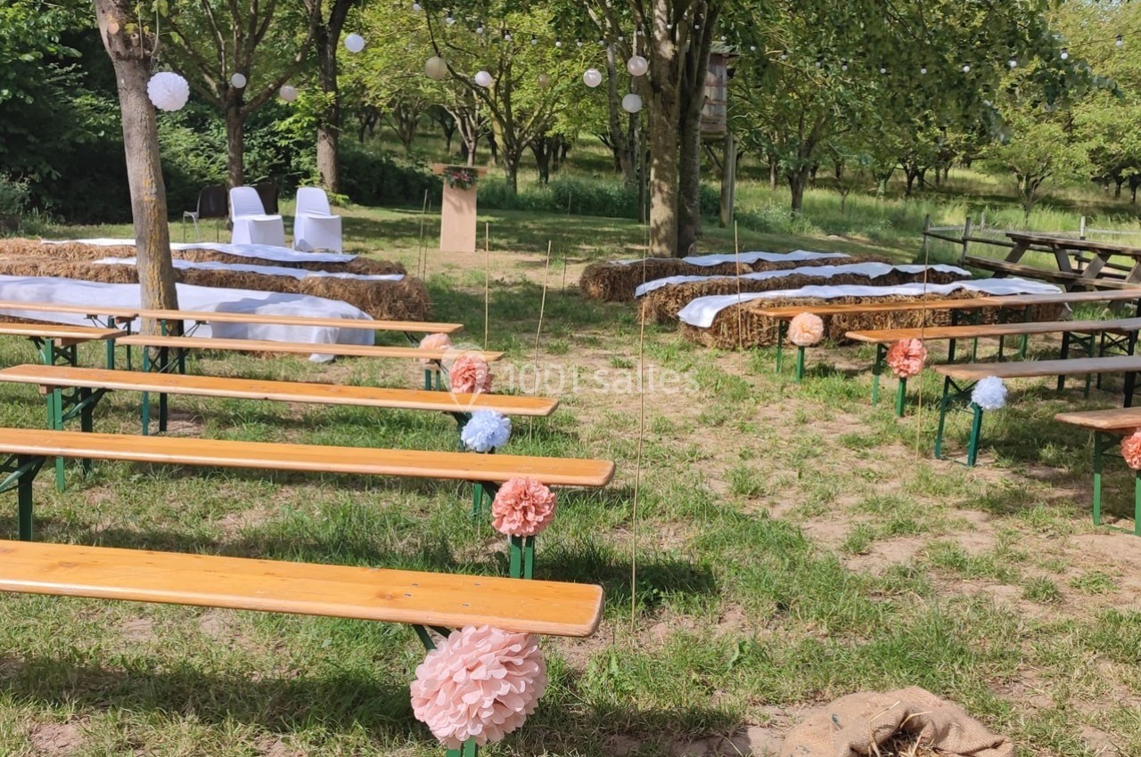 Disposition d'une cérémonie en plein air avec bancs en bois, bottes de paille décorées et allée centrale ornée de pompons…
