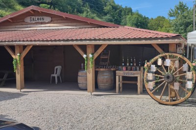 Tente tipi beige installée dans un champ verdoyant sous un ciel bleu, avec une ouverture laissant entrevoir l'intérieur.