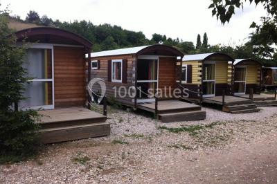 Tente tipi beige installée dans un champ verdoyant sous un ciel bleu, avec une ouverture laissant entrevoir l'intérieur.