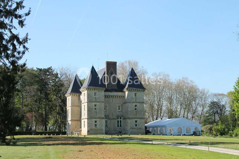Château en pierre entouré d'arbres, avec une grande tente blanche installée sur la pelouse à droite.