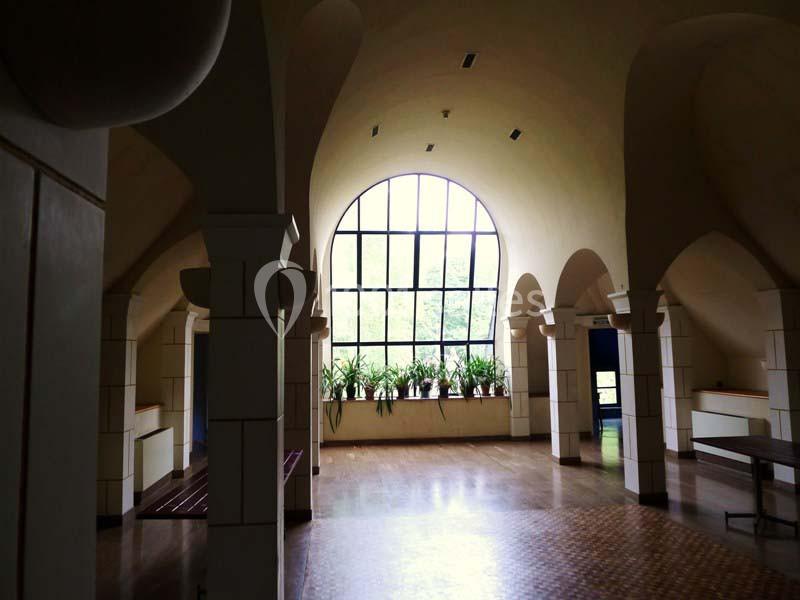 Intérieur lumineux avec de grandes arches, un sol en carrelage et une fenêtre cintrée donnant sur des plantes.