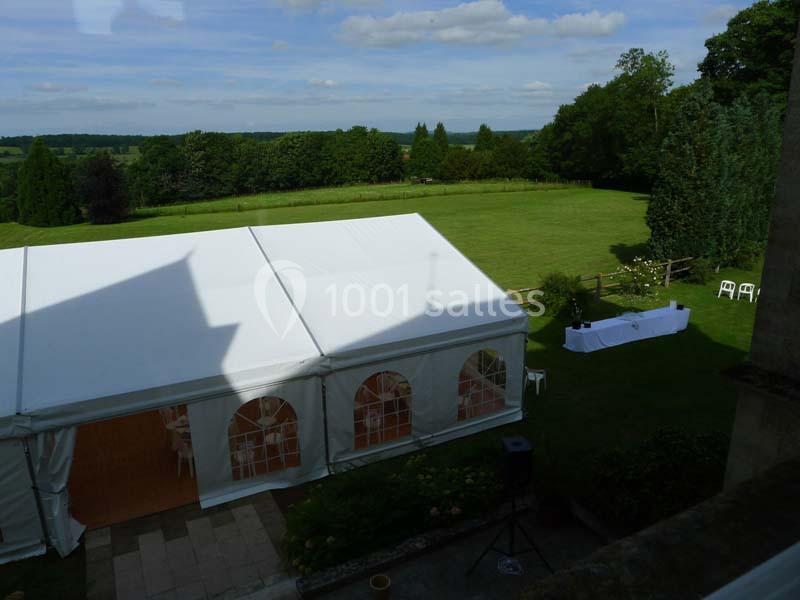 Vue d'une tente blanche installée dans un jardin verdoyant avec une table dressée en arrière-plan.