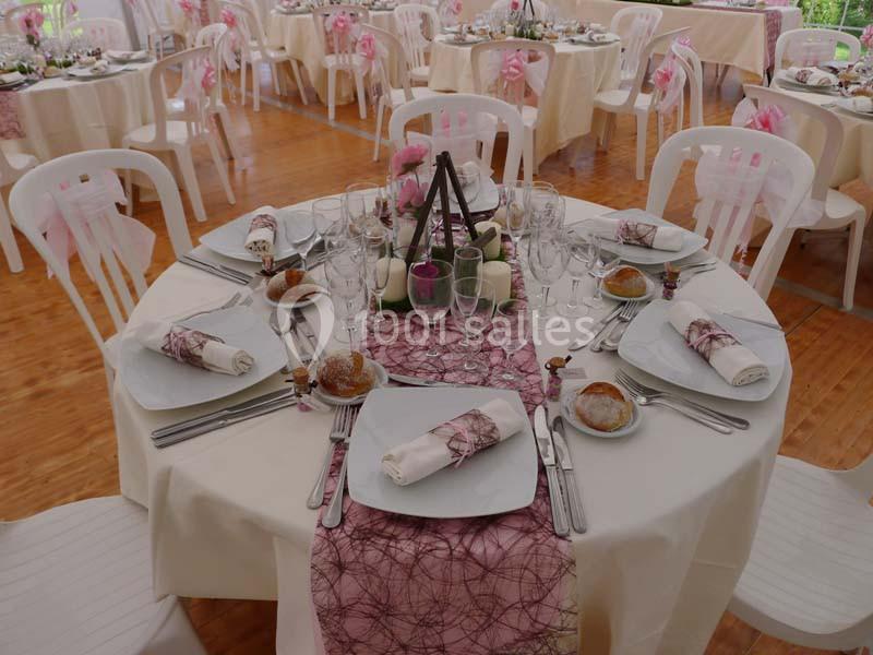 Table de réception élégamment dressée avec nappes blanches, chemins de table roses, vaisselle et décorations florales.