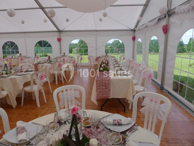 Salle de réception sous chapiteau, tables décorées avec nappes blanches et roses, vue sur un espace vert extérieur.