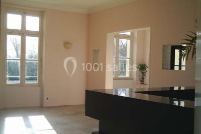 Comptoir d'accueil noir brillant dans un espace lumineux avec un sol en pierre et une plante en pot près d'une fenêtre.