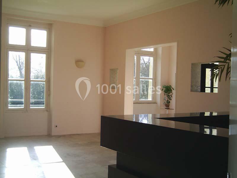 Intérieur lumineux avec murs clairs, grandes fenêtres laissant entrer la lumière et un comptoir noir au premier plan.