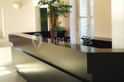 Comptoir d'accueil noir brillant dans un espace lumineux avec un sol en pierre et une plante en pot près d'une fenêtre.