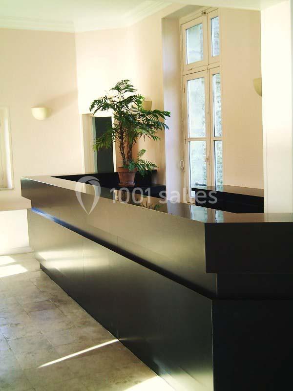 Comptoir d'accueil noir brillant dans un espace lumineux avec un sol en pierre et une plante en pot près d'une fenêtre.