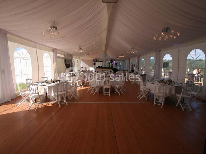 Intérieur d'une tente de réception avec tables rondes dressées, chaises blanches et plafond drapé de tissu blanc.
