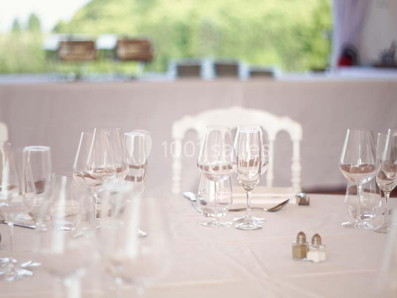 Table élégamment dressée avec des verres à vin, couverts et nappes blanches, en arrière-plan flou.