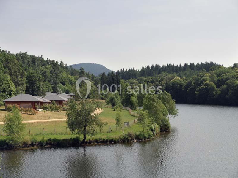 Vue d'un lac bordé de forêt avec des chalets en bois et une clairière sur la rive.