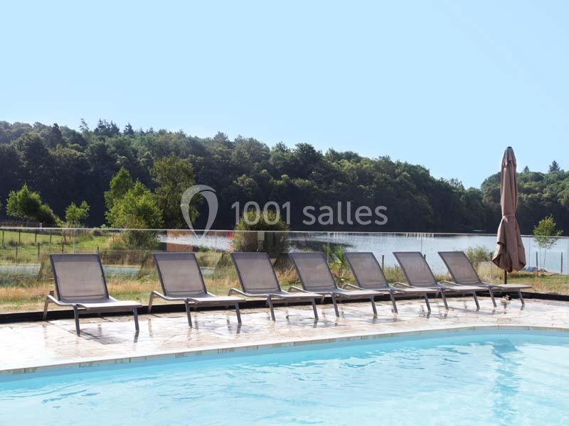 Chaises longues alignées au bord d'une piscine avec vue sur un lac et une forêt en arrière-plan.