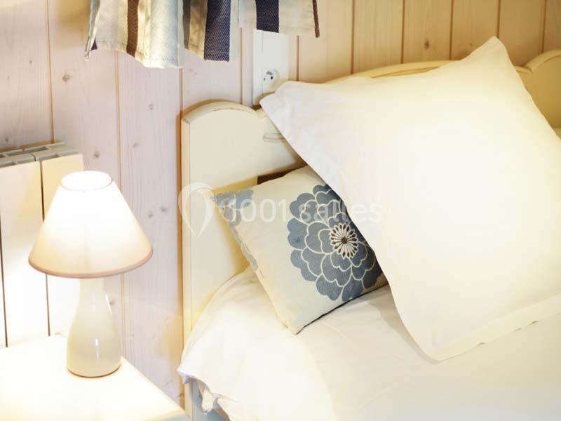 Lampe de chevet allumée près d'un lit avec des coussins décoratifs et une tête de lit en bois clair.