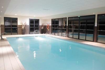 Lavabo avec plan en bois, sèche-serviettes mural, douche avec paroi vitrée et carrelage sombre.