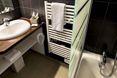 Lavabo avec plan en bois, sèche-serviettes mural, douche avec paroi vitrée et carrelage sombre.