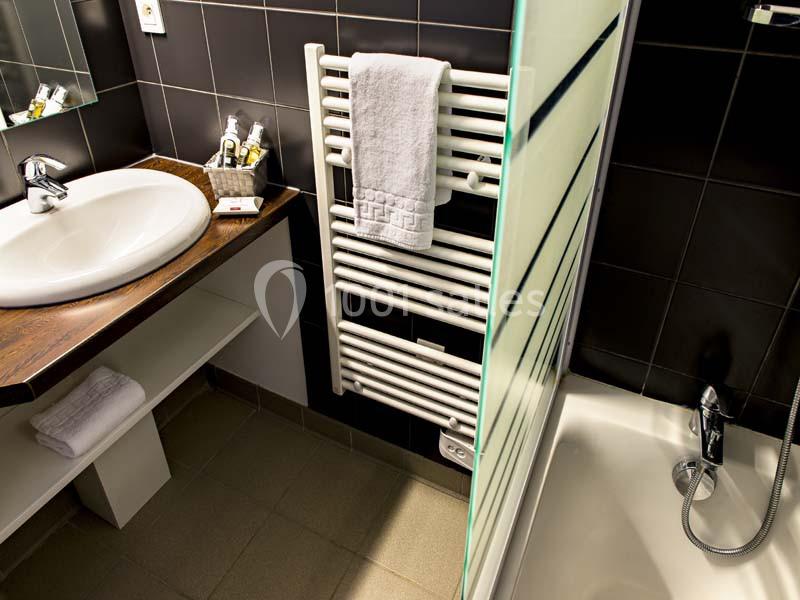 Lavabo avec plan en bois, sèche-serviettes mural, douche avec paroi vitrée et carrelage sombre.