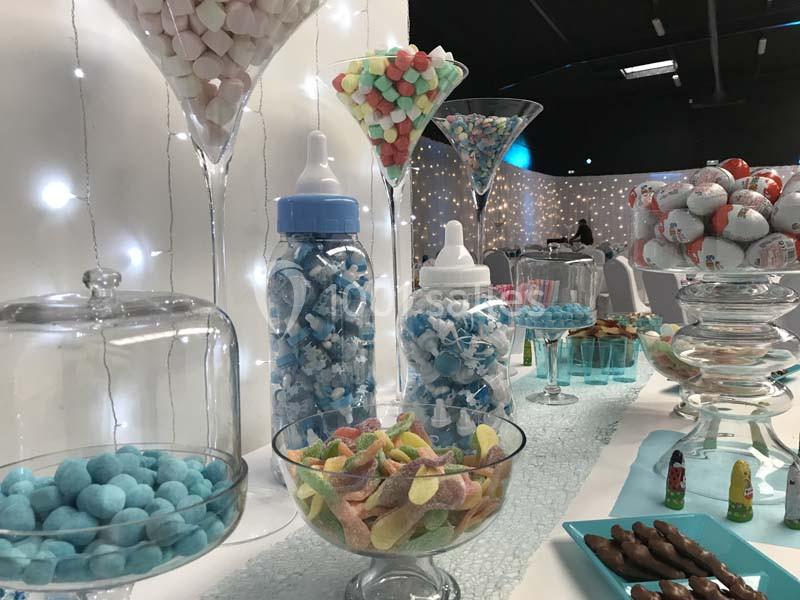 Buffet de bonbons colorés disposés dans des contenants en verre, avec une décoration lumineuse en arrière-plan.