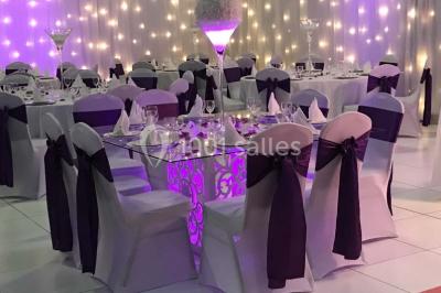 Salle de conférence avec des rangées de chaises vides, éclairée par des guirlandes lumineuses sur les murs.