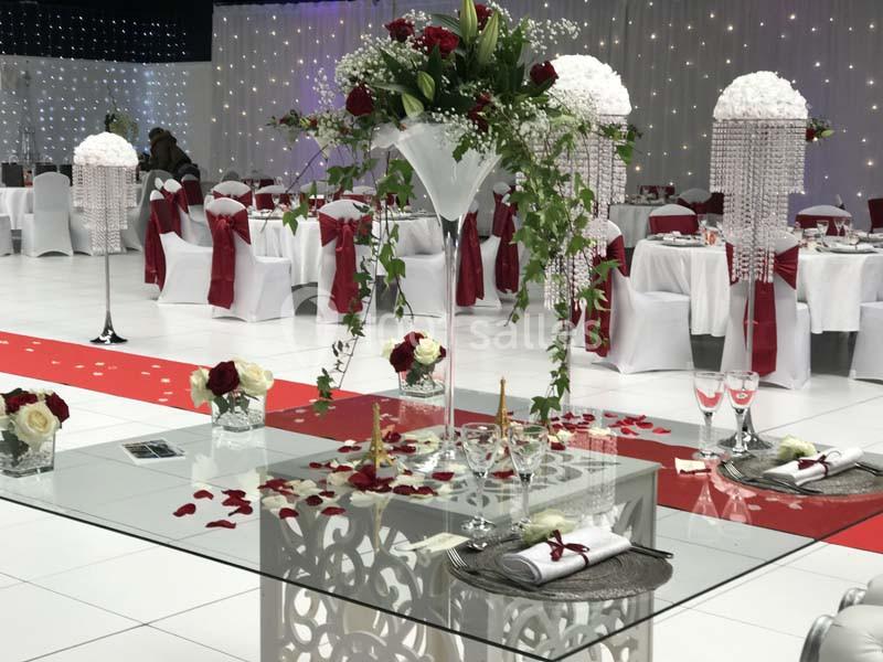 Salle de réception décorée avec des tables élégantes, des chaises blanches ornées de rubans rouges et des centres de table…