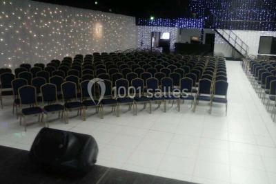 Salle de conférence avec des rangées de chaises vides, éclairée par des guirlandes lumineuses sur les murs.