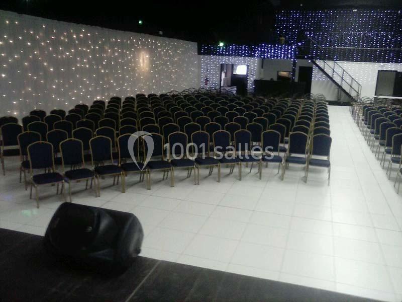 Salle de conférence avec des rangées de chaises vides, éclairée par des guirlandes lumineuses sur les murs.