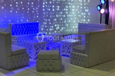 Salle de conférence avec des rangées de chaises vides, éclairée par des guirlandes lumineuses sur les murs.