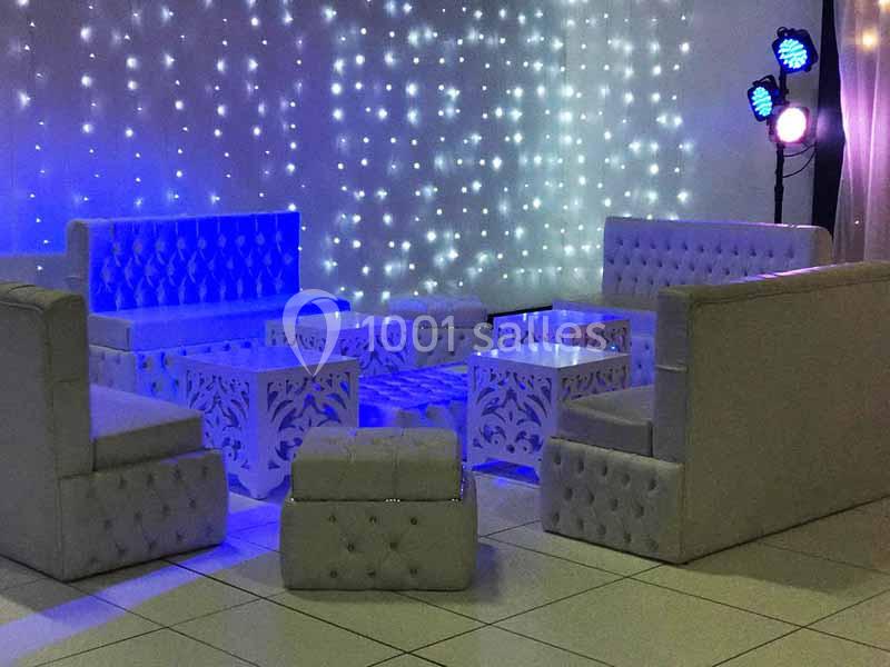 Mobilier blanc capitonné avec tables décoratives, éclairé par des lumières LED et projecteurs colorés.