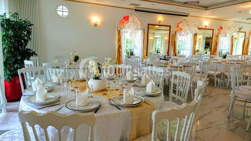Salle de réception élégante avec tables rondes dressées, nappes blanches, chaises assorties et décorations florales.