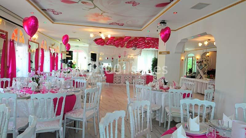 Salle de réception décorée en rose et blanc avec des ballons, des tables dressées et un éclairage chaleureux.