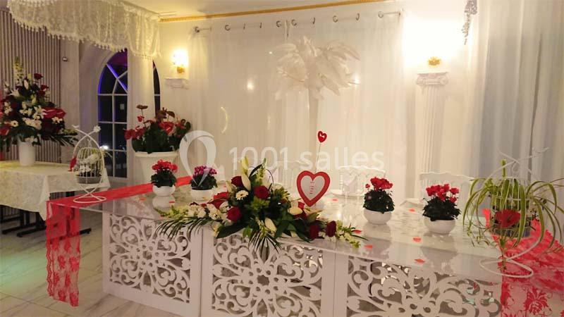 Salle décorée pour un événement avec table ornée de fleurs, motifs ajourés, et rideaux blancs en arrière-plan.