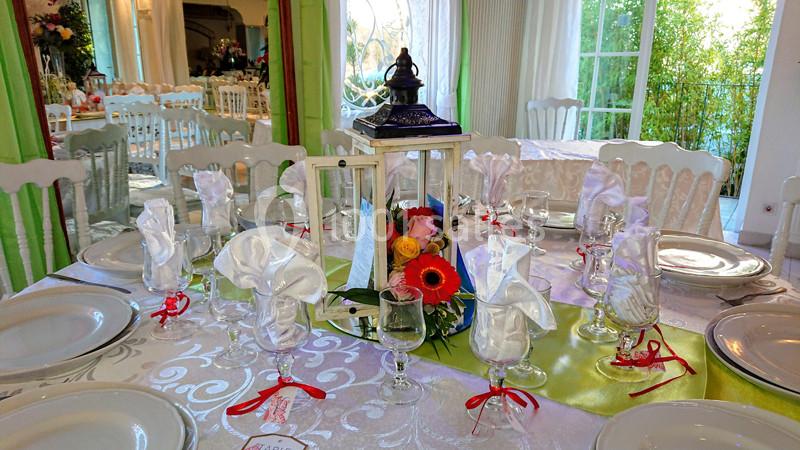 Table dressée avec nappes blanches, serviettes pliées, lanternes décoratives et fleurs colorées dans une salle lumineuse.