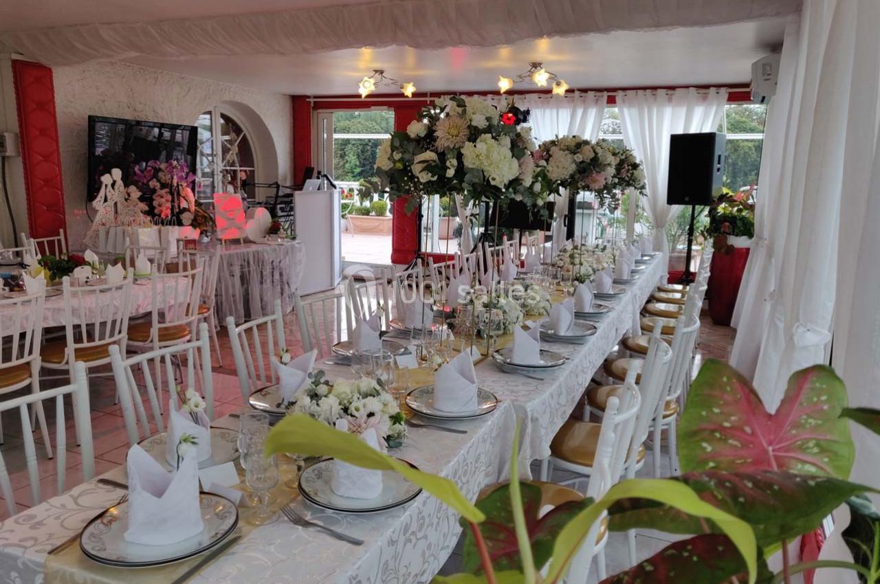Salle décorée pour un événement avec une longue table dressée, ornée de fleurs blanches et de serviettes pliées.