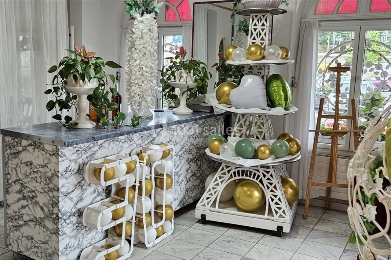 Décoration intérieure avec comptoir en marbre, plantes, ballons dorés et blancs disposés sur une structure décorative.